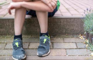 ein Junge mit kaputten Schuhen auf einer Treppe